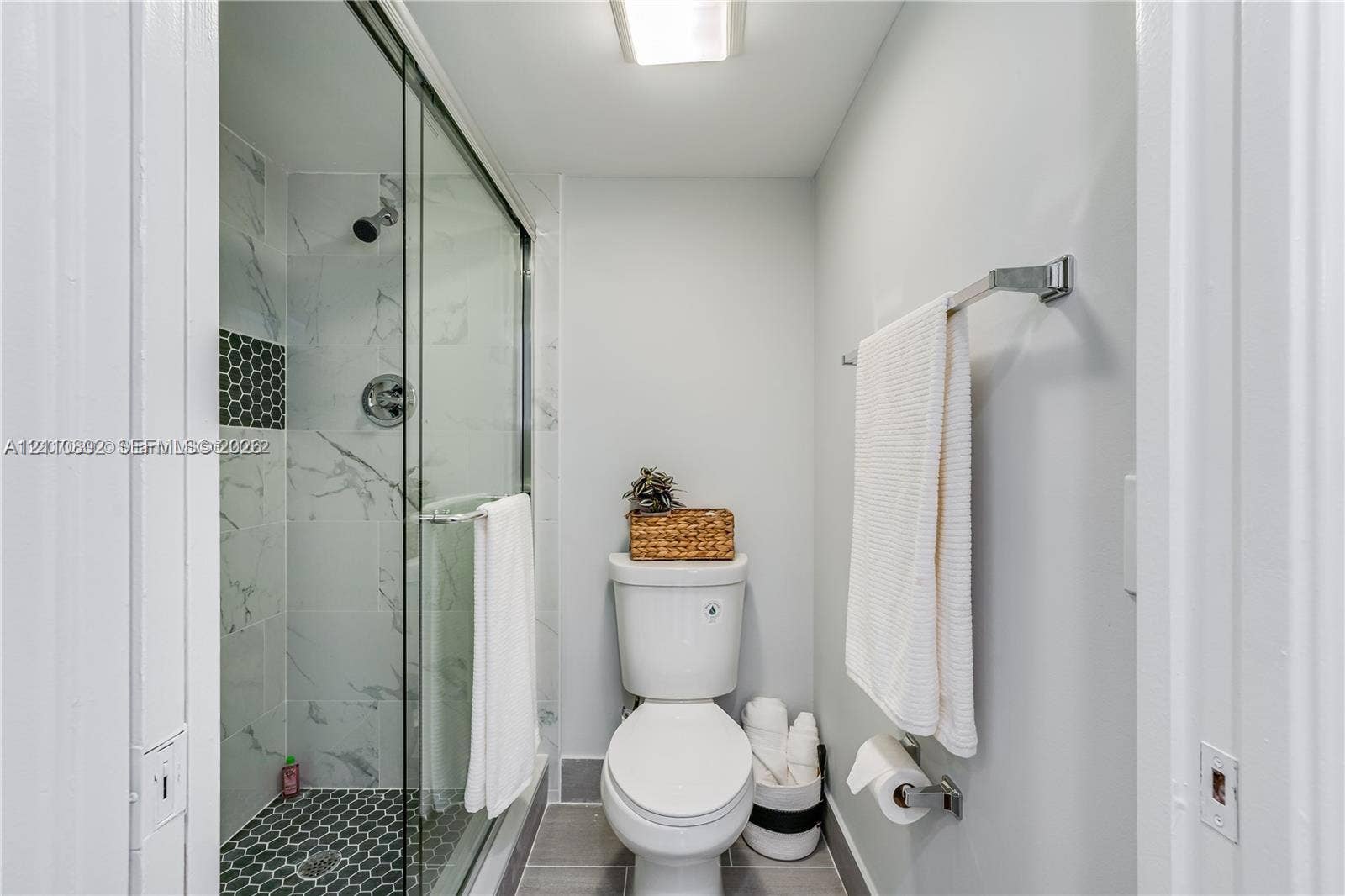 Walk-in shower with glass enclosure, large-format tile wall surround, geometric floor tiling, and a metal towel rack