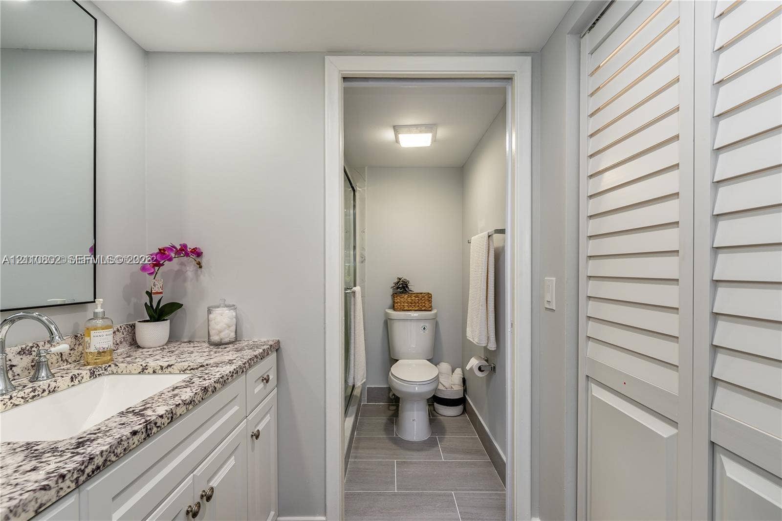 Vanity featuring a stone-look countertop, integrated sink with chrome faucet, framed mirror, and louvered closet doors