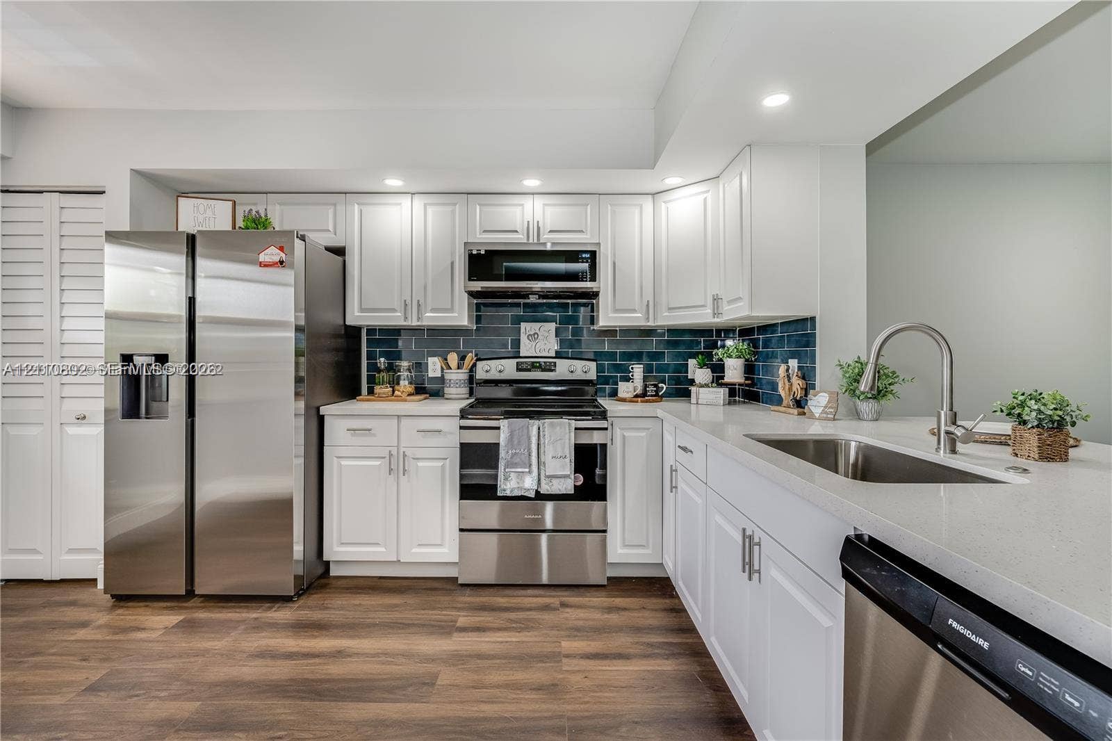 Kitchen featuring white shaker-style cabinetry, stainless steel appliances, dark subway-tile backsplash, stone-finish countertops, and wood-finish flooring