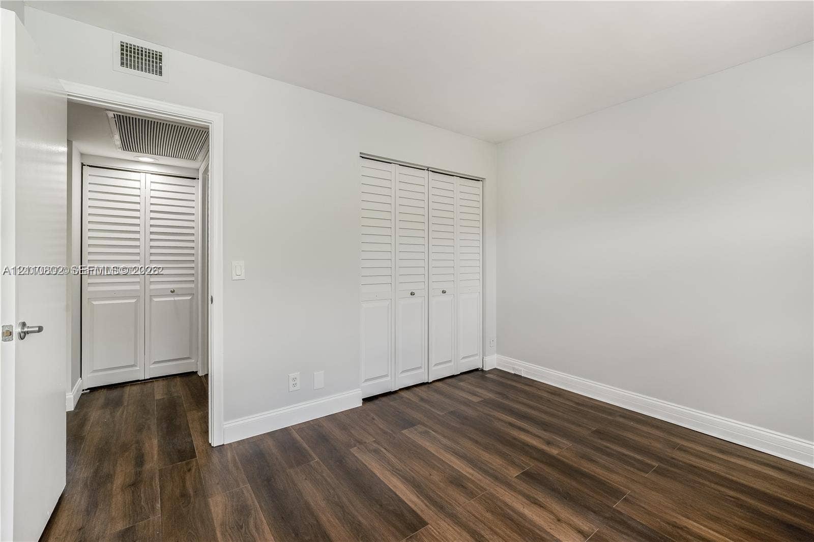 Room interior featuring wood-finish flooring, white walls, and two sets of white louvered-panel closet doors