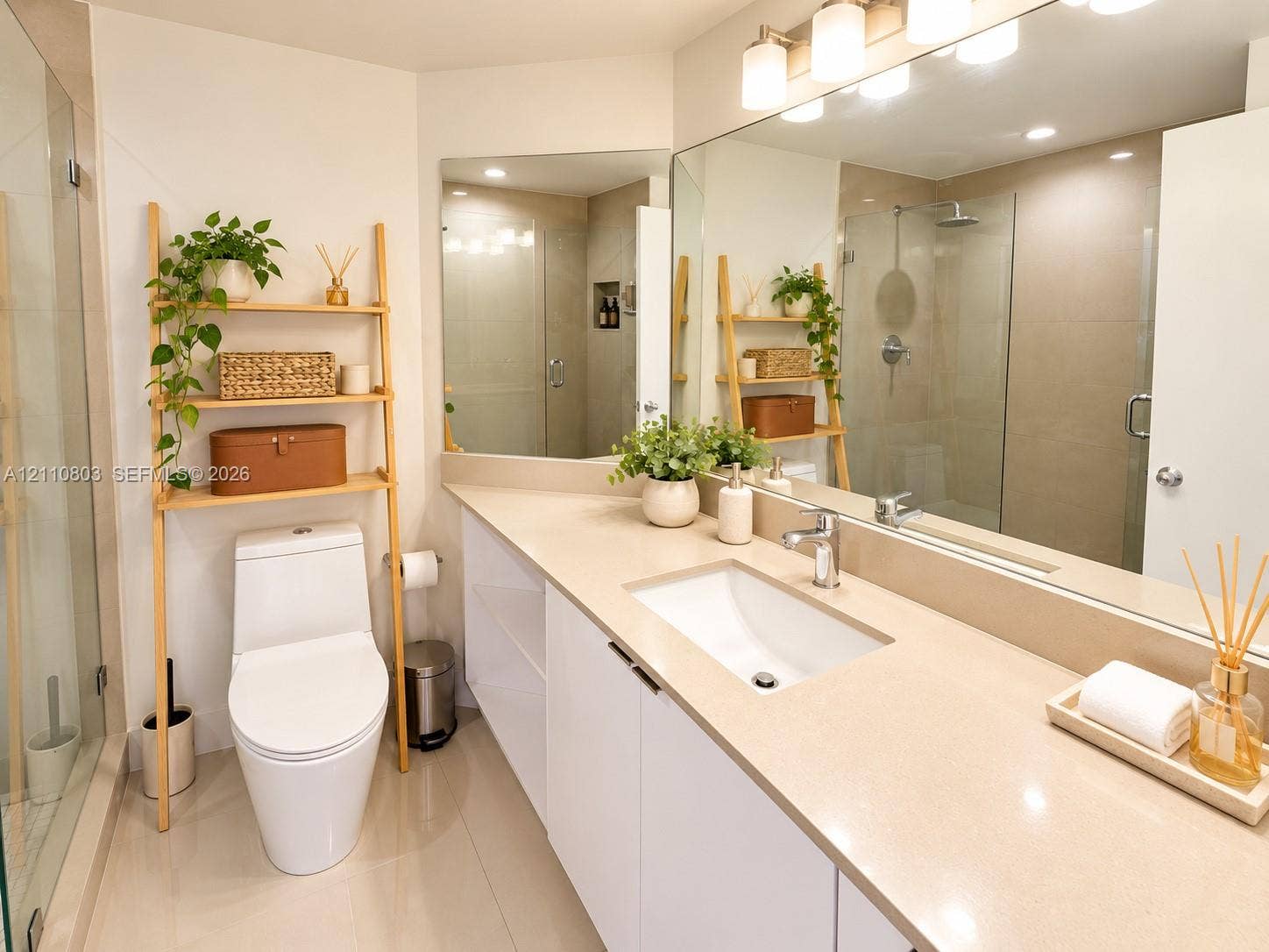 Bathroom vanity with a neutral solid-surface countertop and integrated sink, complemented by a large wall-mounted mirror, three-light fixture, glass-enclosed shower, and tile flooring