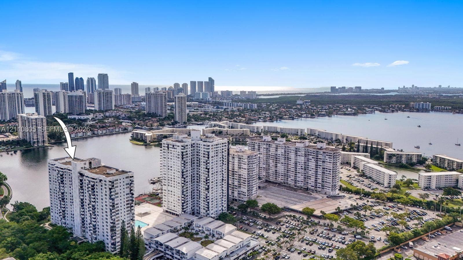 High-rise residential building featuring expansive water frontage, open-air balconies, and a surface parking lot