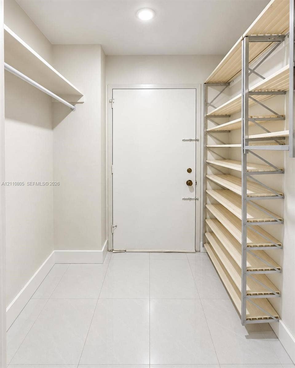 Storage space featuring floor-to-ceiling multi-tiered wooden shelving, white tile flooring, recessed ceiling lighting, and a neutral color palette