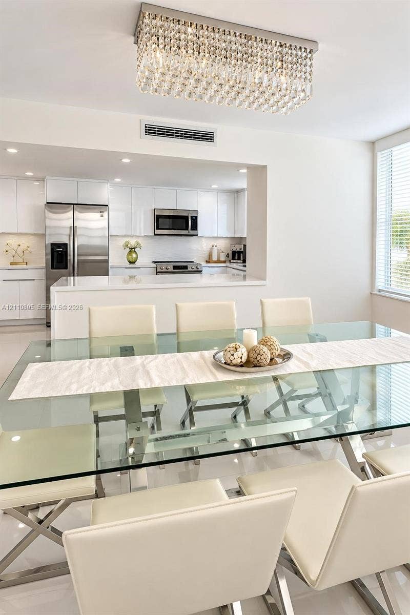 Modern dining area featuring a tiered crystal chandelier, glossy tile flooring, and clean-lined cabinetry in the kitchen