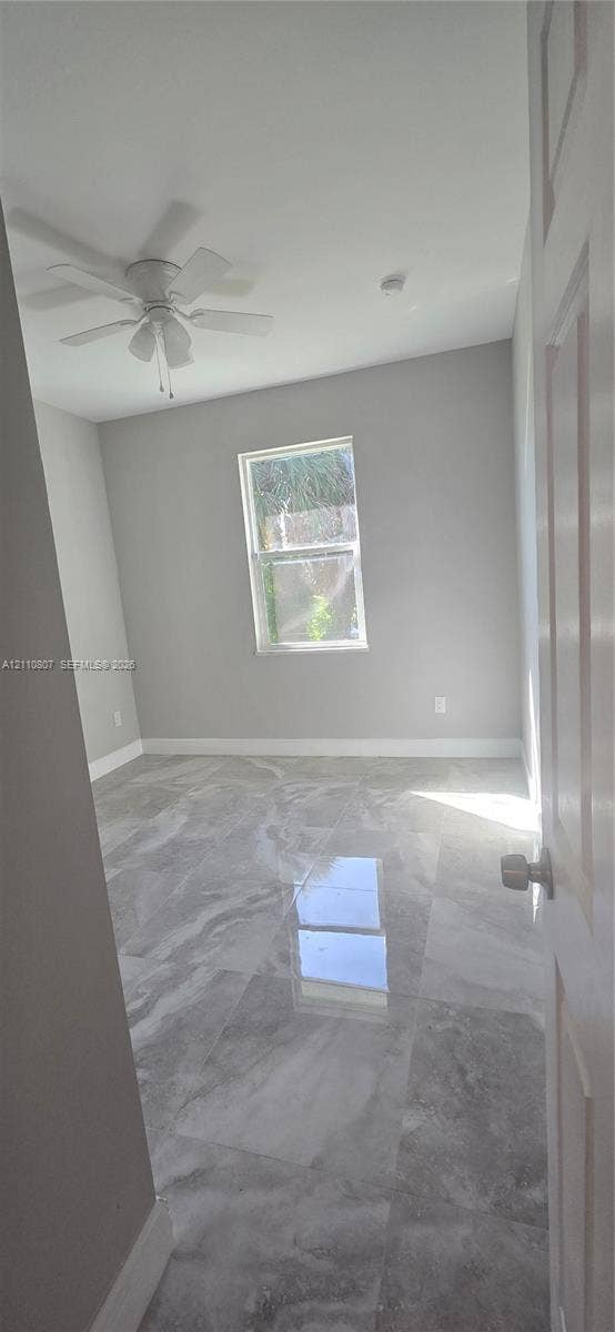 Polished stone-finish flooring, neutral wall tones, single-pane window, and white ceiling fan with integrated lighting