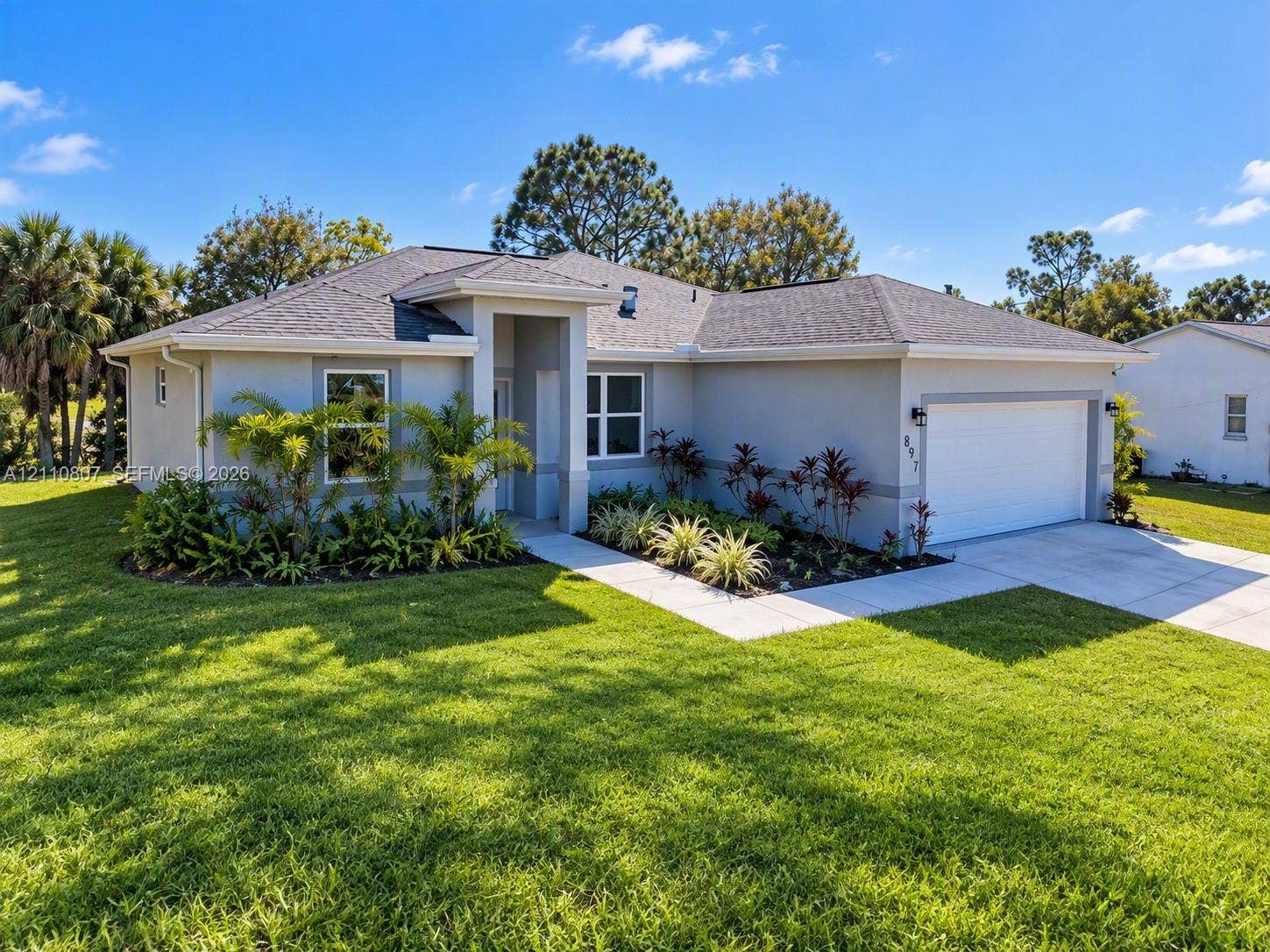 Single-story residence featuring a neutral stucco exterior, a concrete driveway, a two-car garage, and a hip roofline, set within a landscaped lawn