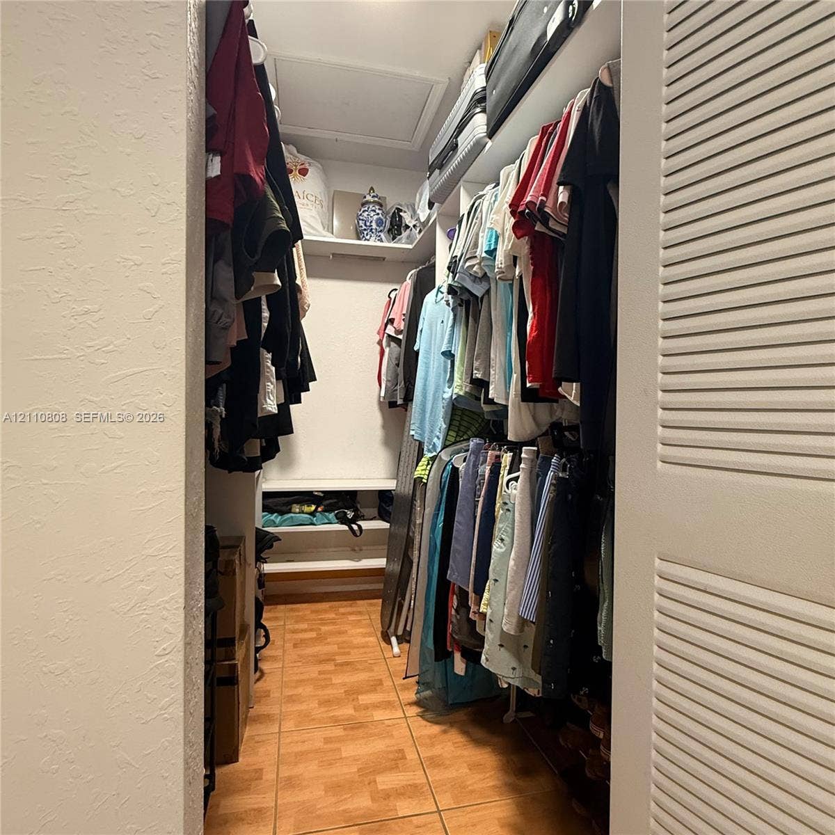 Reach-in closet featuring ceramic tile flooring, built-in shelving, and louvered double doors