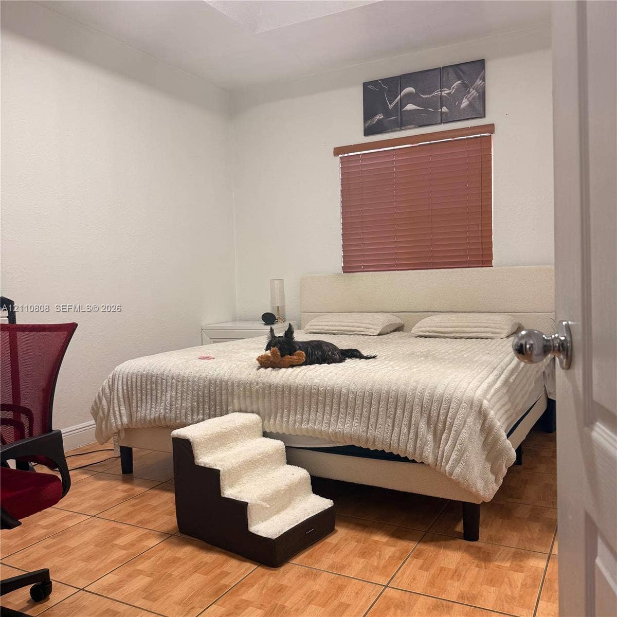 Room featuring ceramic tile flooring, tray ceiling, and a window equipped with horizontal slat blinds