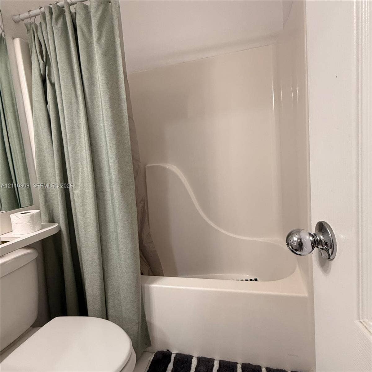 Integrated white acrylic tub and wall surround featuring a chrome-finish door knob