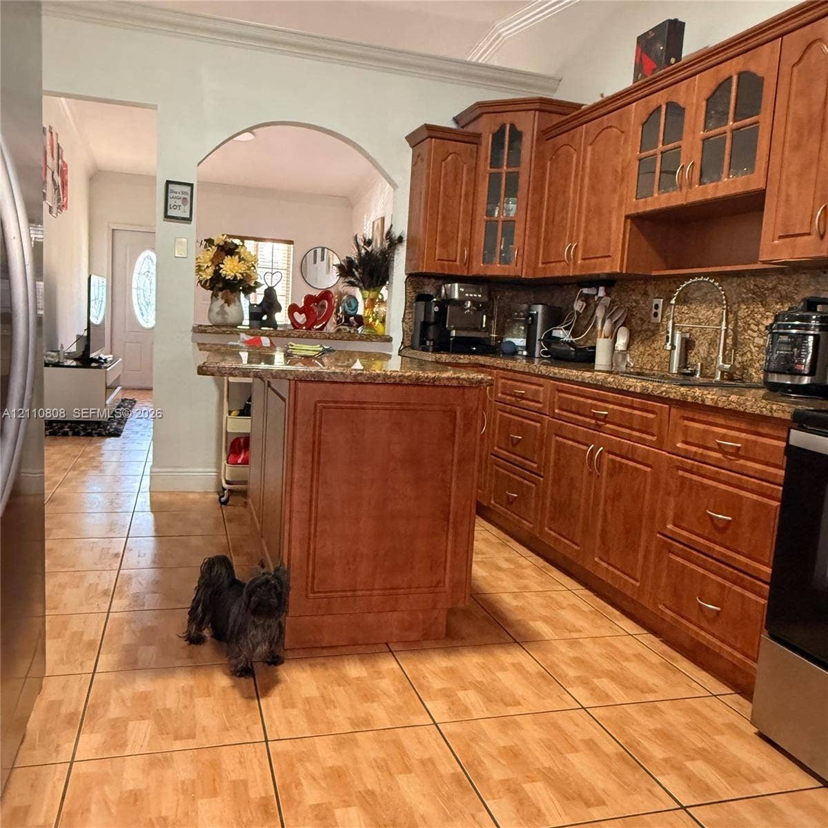 Kitchen featuring stained wood cabinetry, stone countertops, central island, tiled flooring, and arched entryway