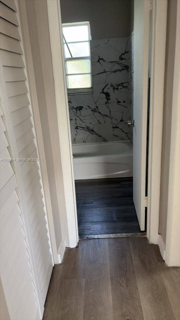Wood-finish flooring, white louvered closet doors, and a bathroom featuring a shower-tub combination with large-format veined wall tile