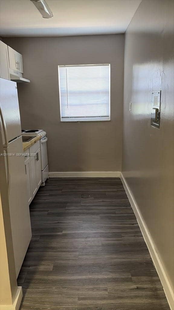 Kitchen featuring wood-finish flooring, white cabinetry, a built-in electric range, and a refrigerator