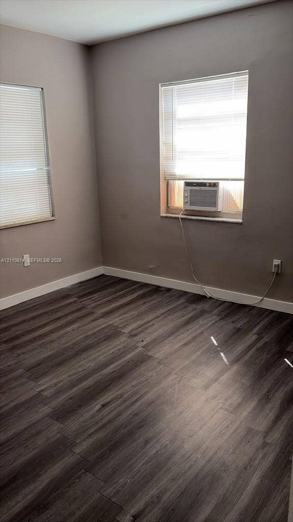 Neutral-toned room featuring wood-finish flooring, two windows with horizontal blinds, and a wall-mounted air conditioning unit