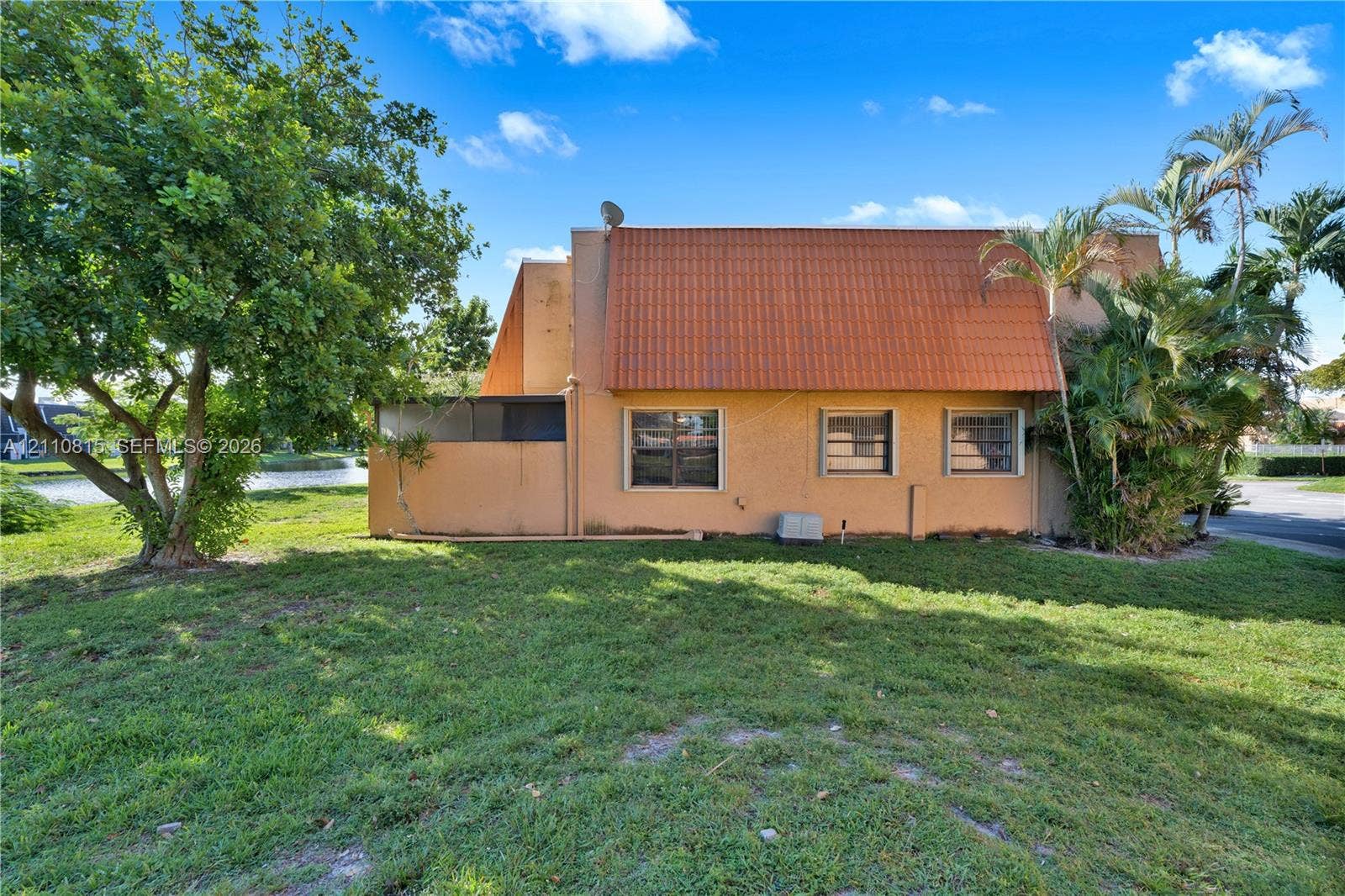 9100 Orchid Tree Lane, #137, Pembroke Pines, FL 33024 Stucco exterior featuring a dual-pitch clay tile roof, horizontal sliding windows, and an expansive lawn with mature trees