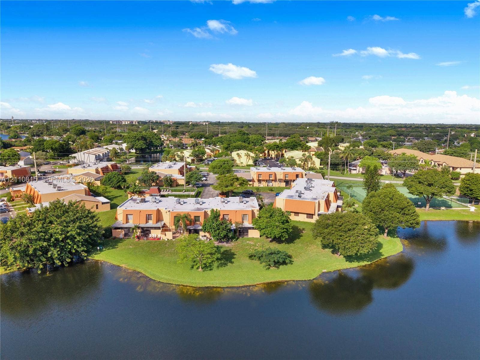 9100 Orchid Tree Lane, #137, Pembroke Pines, FL 33024 Aerial perspective featuring waterfront grounds, mature trees, expansive manicured lawn, and on-site recreational court