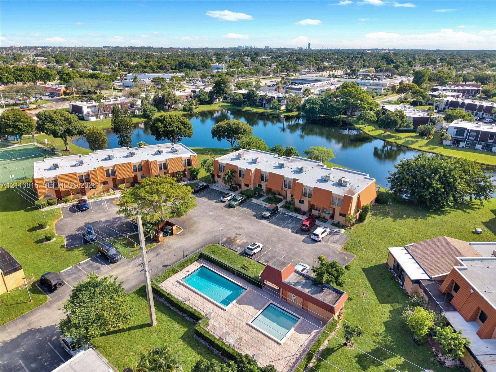 9100 Orchid Tree Lane, #137, Pembroke Pines, FL 33024 Aerial perspective of multi-unit residential buildings featuring a community swimming pool, paved surface parking, and waterfront grounds