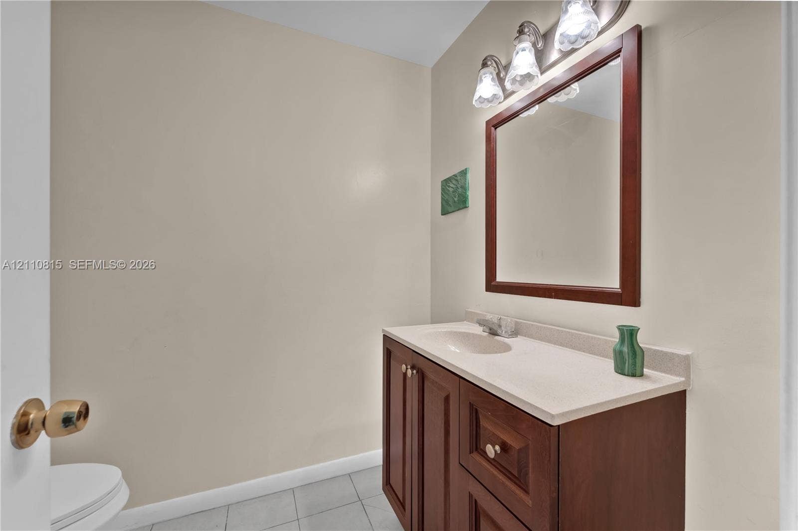 9100 Orchid Tree Lane, #137, Pembroke Pines, FL 33024 Bathroom featuring a wood-finish vanity with a stone-surface countertop, an integrated sink, a framed mirror, and a three-bulb light fixture