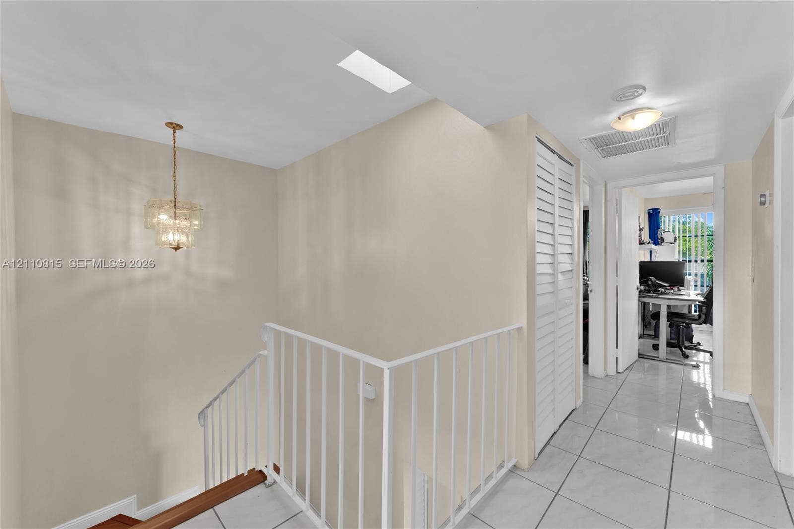 9100 Orchid Tree Lane, #137, Pembroke Pines, FL 33024 Interior hall featuring white tile flooring, ceiling-mounted crystal chandelier, skylight, and white louvered closet doors with a metal railing