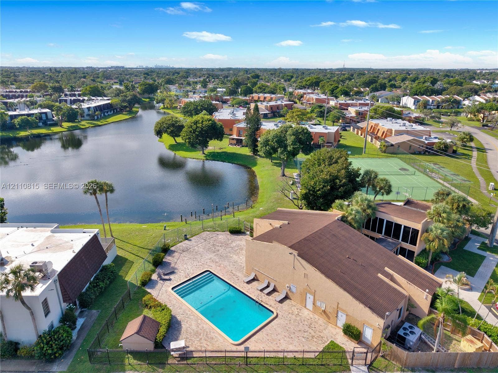 9100 Orchid Tree Lane, #137, Pembroke Pines, FL 33024 Aerial perspective of a community featuring a swimming pool with paver decking, a tennis court, a pond, and mature landscaping