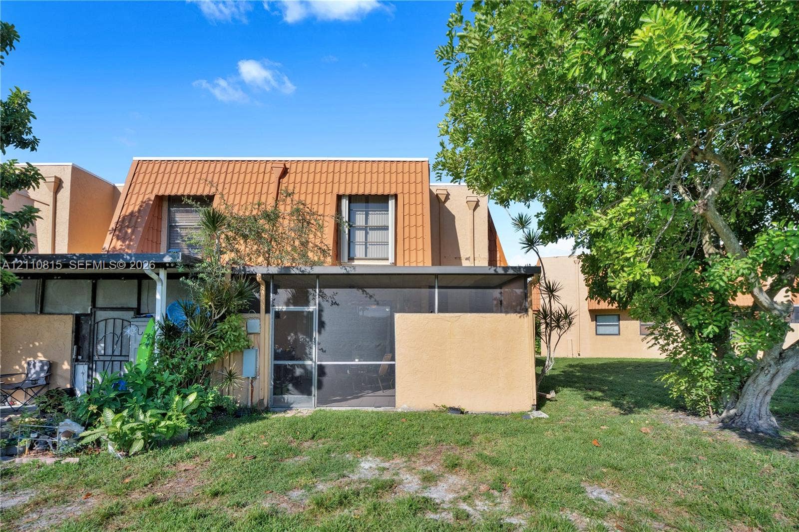 9100 Orchid Tree Lane, #137, Pembroke Pines, FL 33024 Stucco exterior featuring a metal mansard roof, screened-in lanai, and mature landscaping