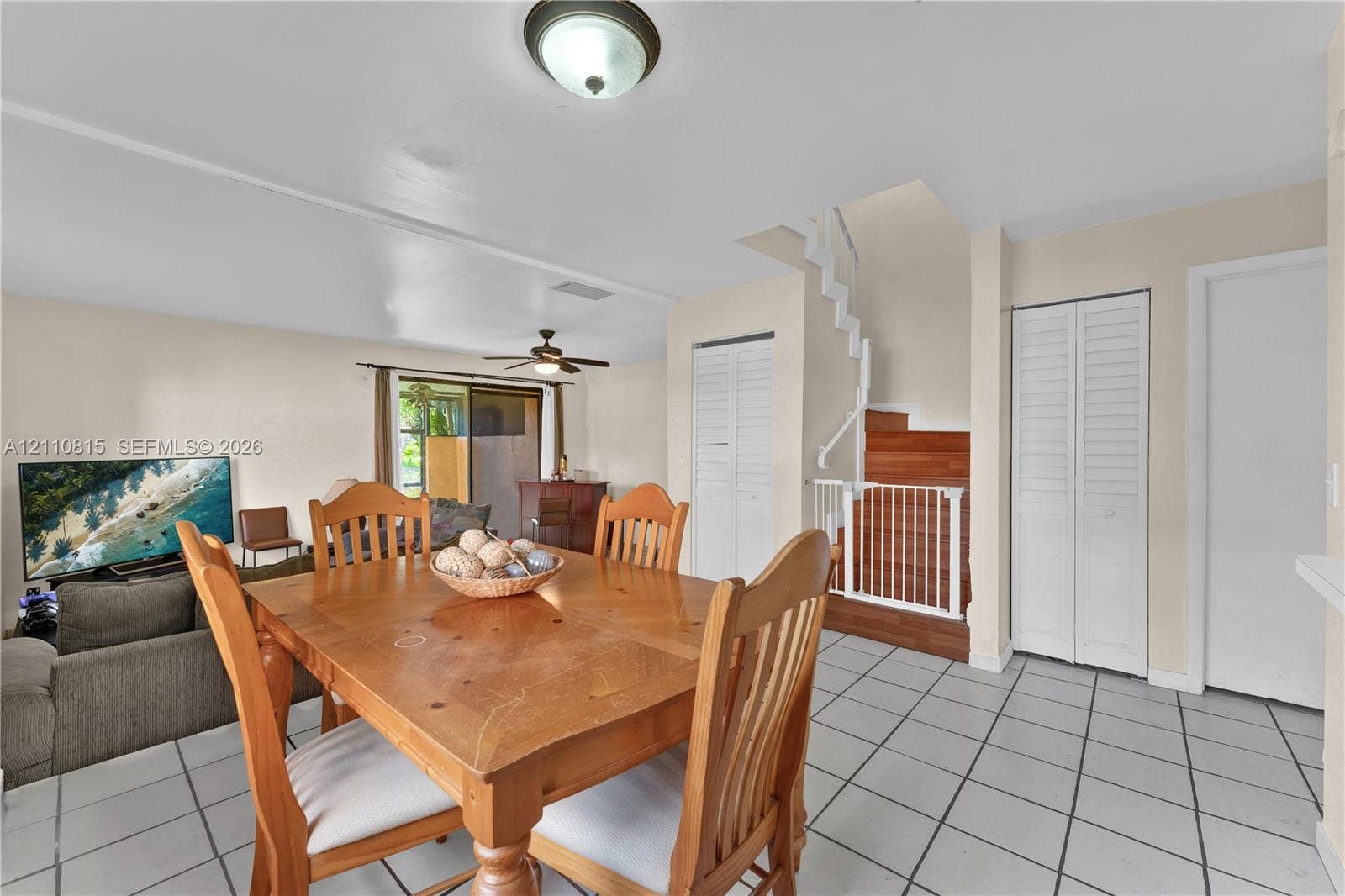 9100 Orchid Tree Lane, #137, Pembroke Pines, FL 33024 Interior area featuring white tile flooring, staircase with wood-finish treads, ceiling fan with light fixture, and dual-closet storage with louvered doors