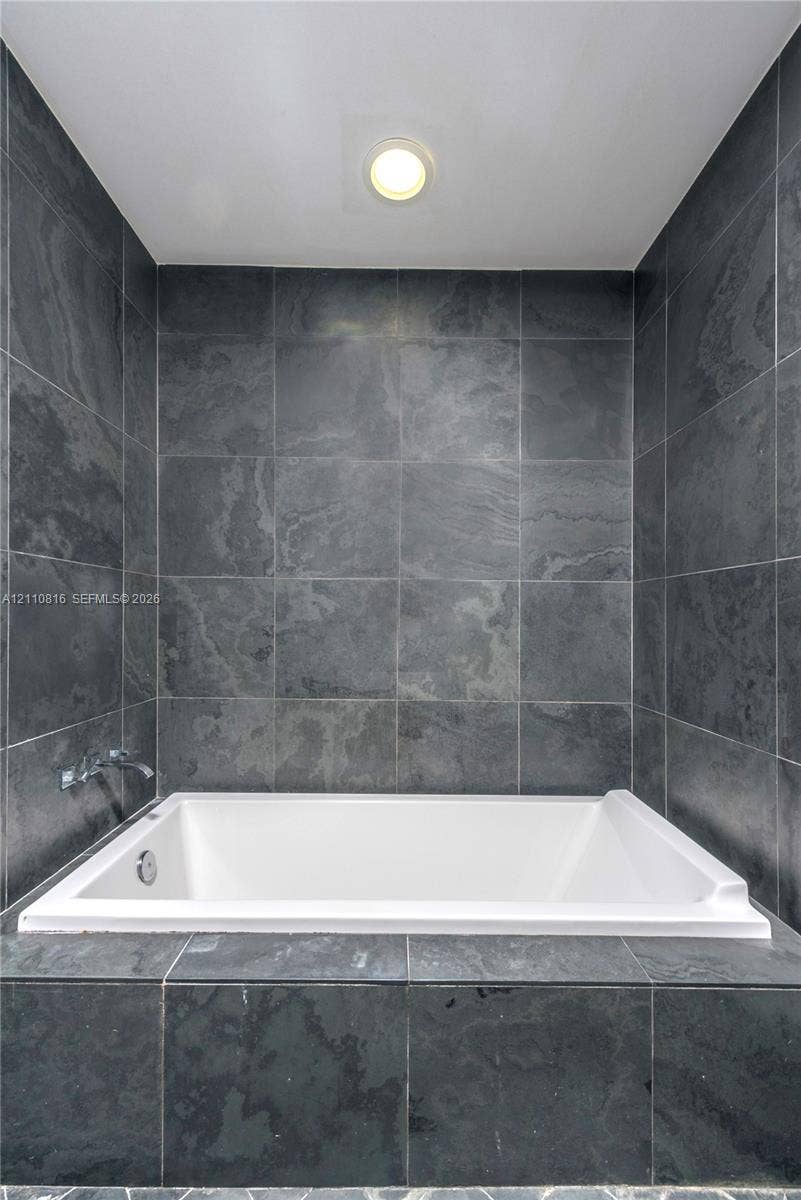 Built-in soaking tub featuring a white acrylic finish, surrounded by charcoal-toned stone tile surround and matching full-height tiled wall accents with integrated chrome faucet hardware