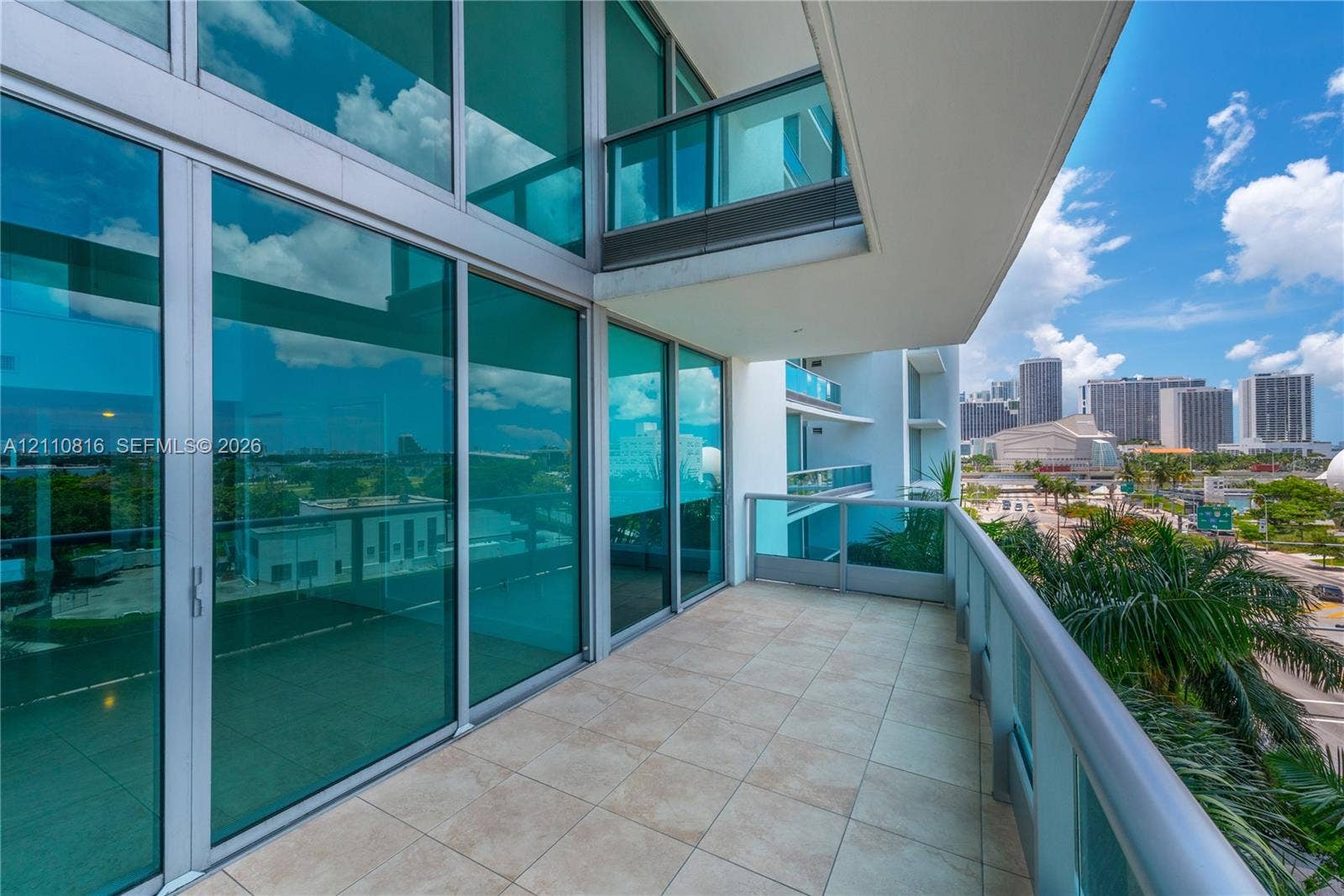 Covered balcony featuring oversized tile flooring, full-height glass sliding doors, and a glass-paneled railing