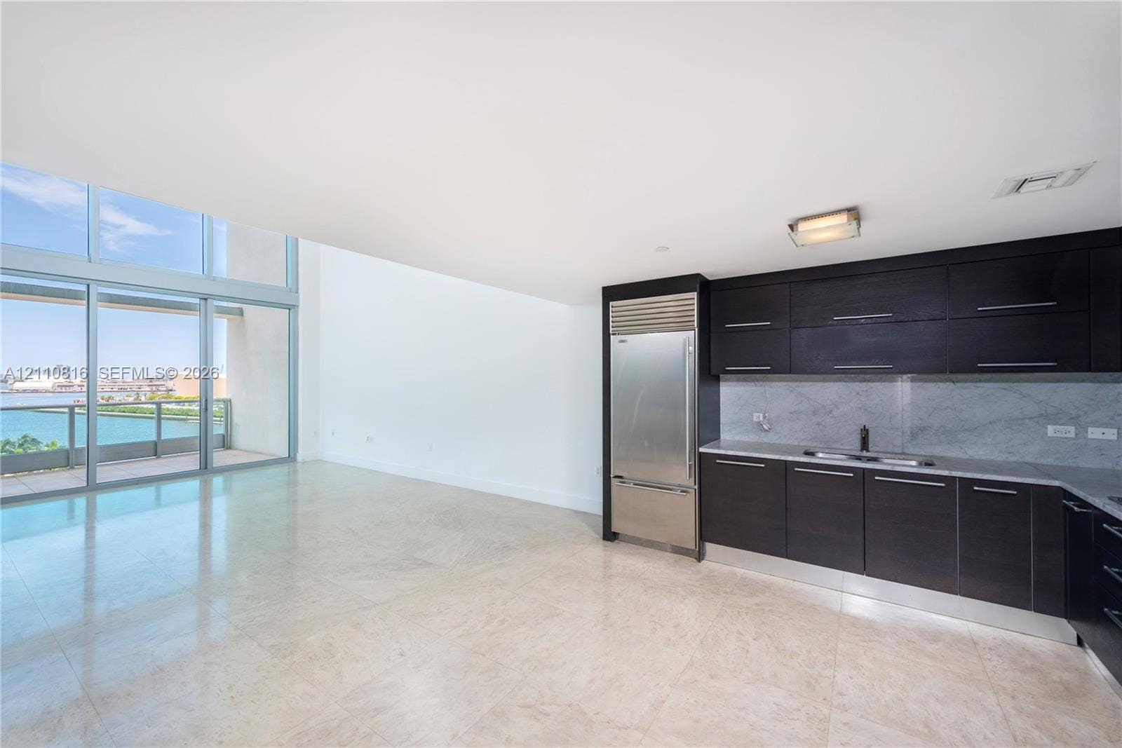 Kitchen featuring dark cabinetry, integrated stainless steel refrigerator, stone-style backsplash, and light-toned flooring, with floor-to-ceiling windows