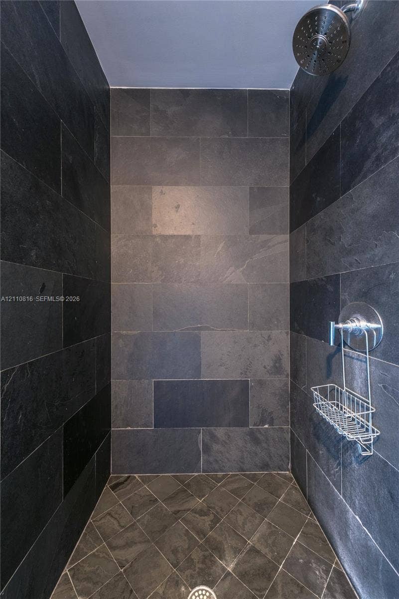 Walk-in shower enclosure featuring full-height charcoal stone tile walls, coordinating diamond-patterned tile flooring, a circular chrome showerhead, and a matching chrome pressure-balance valve