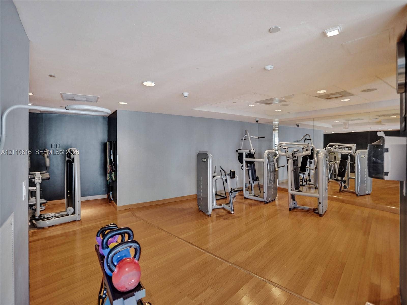 Fitness area featuring wood-finish flooring, recessed lighting, and expansive wall-to-wall mirrors