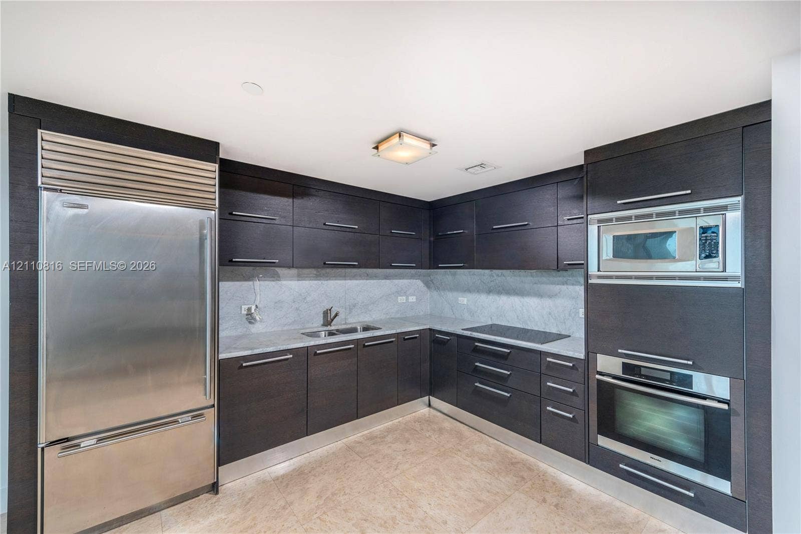 Kitchen featuring dark-toned flat-panel cabinetry, stone countertops, integrated stainless steel refrigerator, built-in microwave, and wall-mounted oven