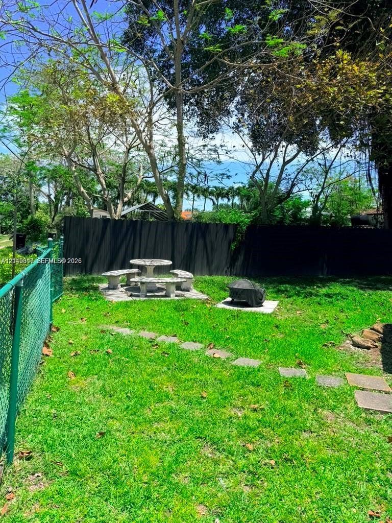 201 Flagler Drive, #201, Miami Springs, Miami Springs, FL 33166 Private backyard featuring a chain-link perimeter fence, dark solid-panel privacy screening, stone paver stepping stones, and mature trees