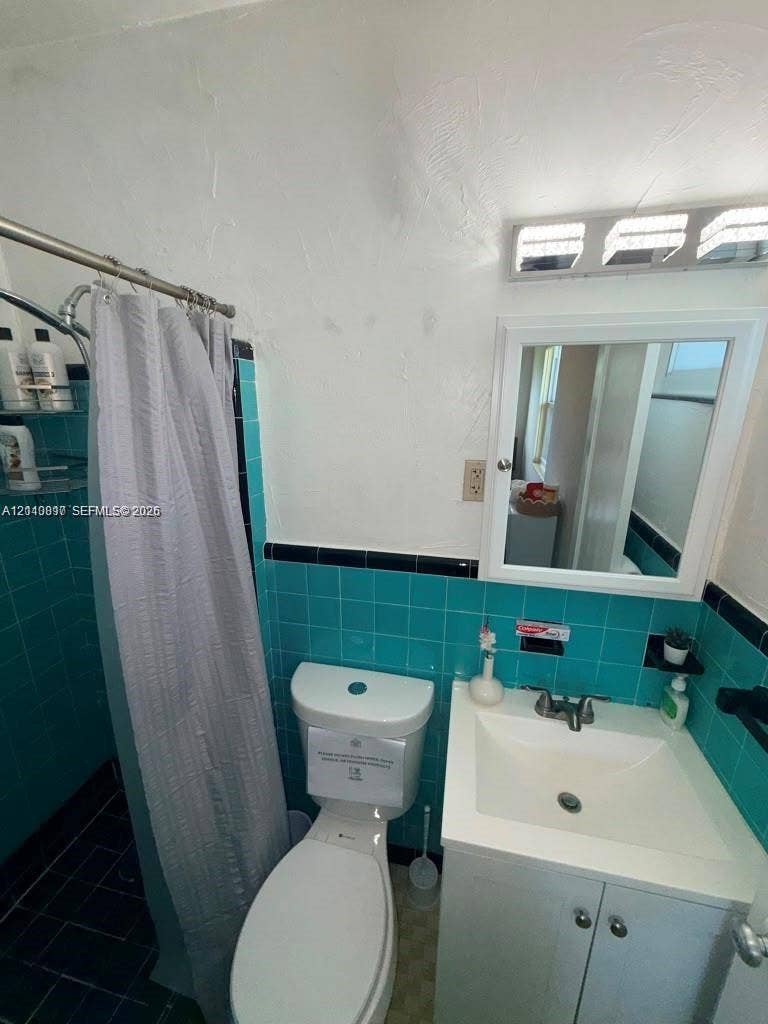 201 Flagler Drive, #201, Miami Springs, Miami Springs, FL 33166 Bathroom featuring teal wall tiling with black accent trim, a white vanity with an integrated sink, a medicine cabinet, and a multi-bulb light fixture