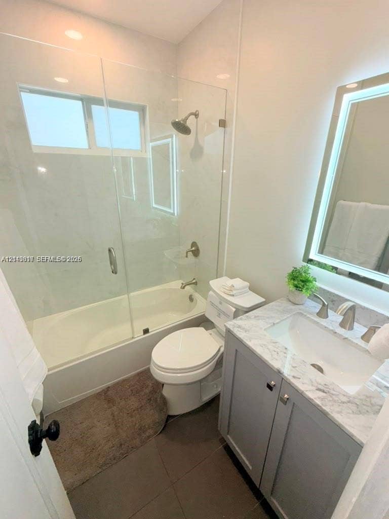 201 Flagler Drive, #201, Miami Springs, Miami Springs, FL 33166 Bathroom featuring a vanity with a stone-top counter, undermount sink, and integrated LED-lit mirror, paired with a glass-enclosed shower and tub combination featuring stone-finish wall tile