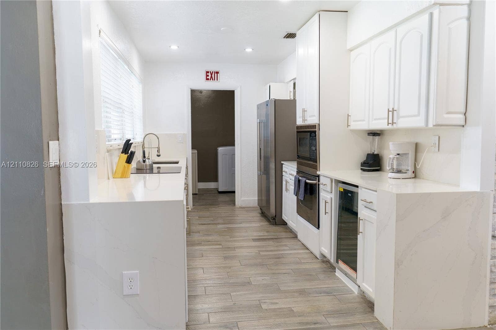 Kitchen featuring white cabinetry, quartz countertops with waterfall edge, wood-finish flooring, stainless steel wall-mounted oven, and recessed lighting