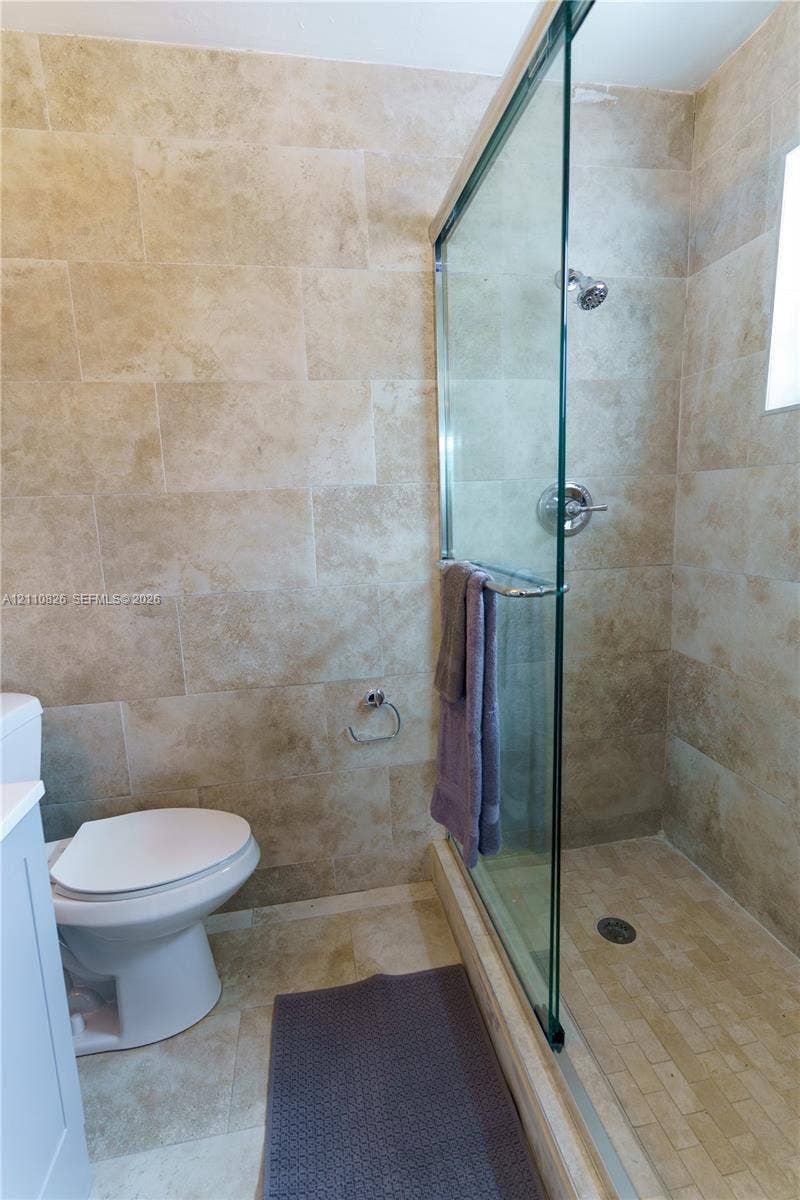 Shower enclosure featuring floor-to-ceiling natural stone tile, glass door, and polished chrome fixtures