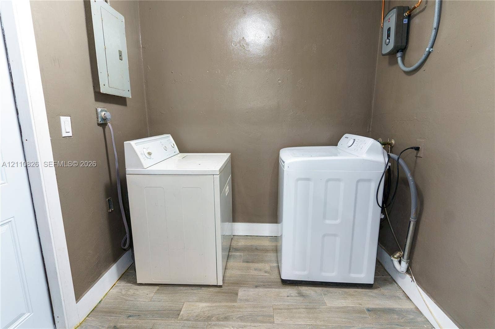Dedicated laundry space featuring wood-finish flooring, integrated electrical panel, and wall-mounted water heater