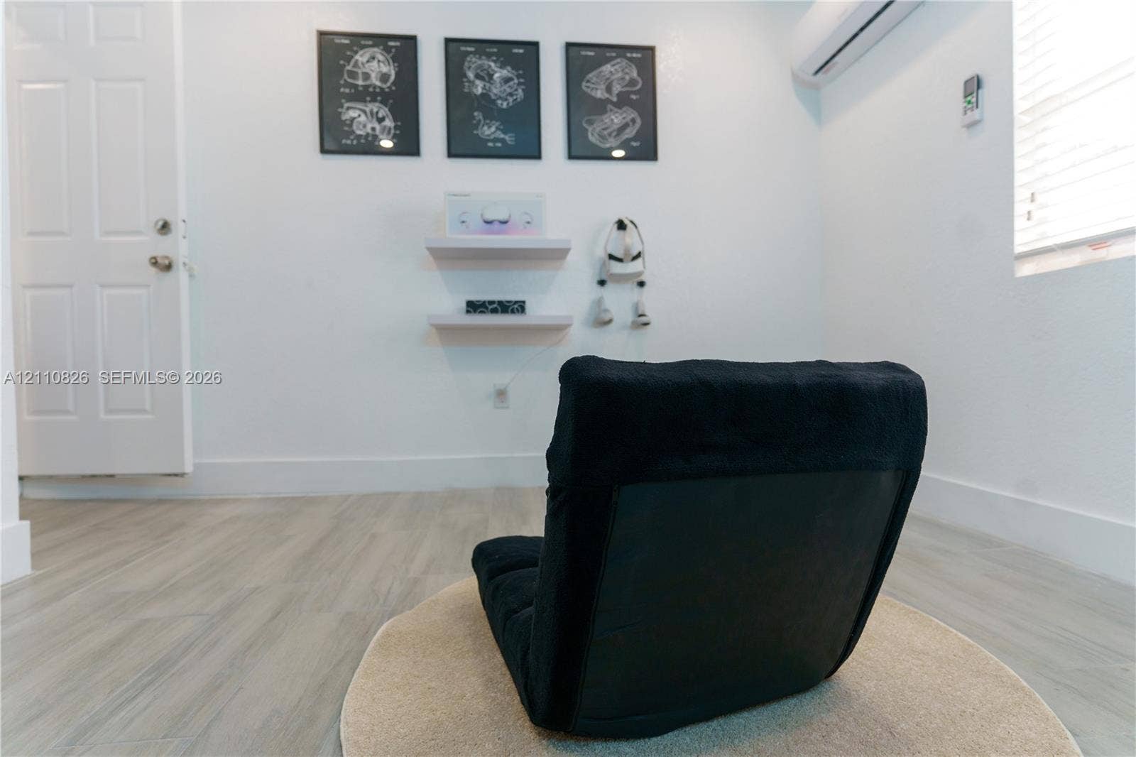 Wood-finish flooring, two wall-mounted floating shelves, white six-panel interior door, and wall-mounted climate control unit