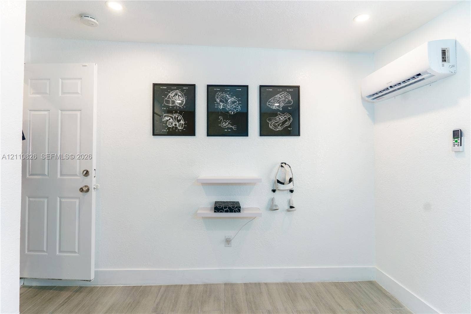 Interior space featuring wood-finish flooring, a wall-mounted ductless mini-split air conditioning unit, recessed ceiling lighting, and two minimalist floating shelves