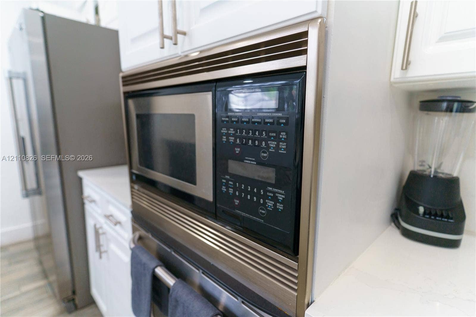 Built-in stainless steel microwave oven, white cabinetry featuring brushed metal hardware, and solid-surface countertops