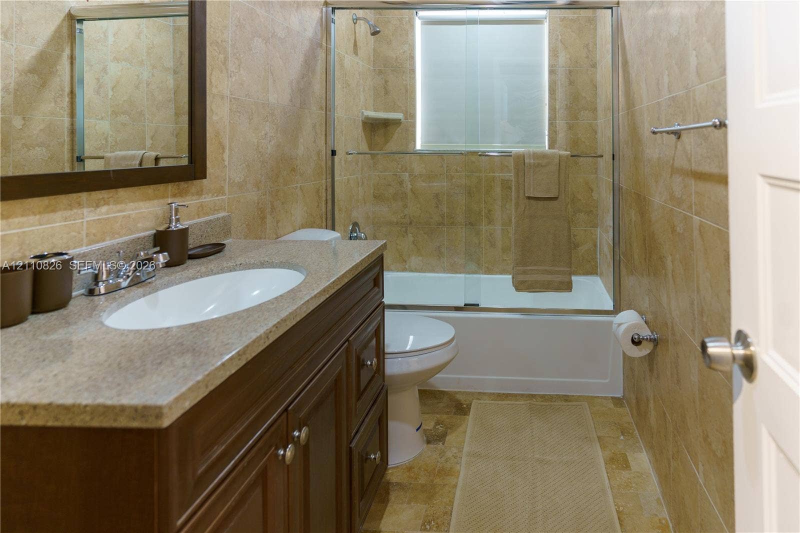 Bathroom featuring a vanity with a stone-finish countertop and an integrated oval sink, full-height stone-tile shower surround, and glass sliding tub enclosure
