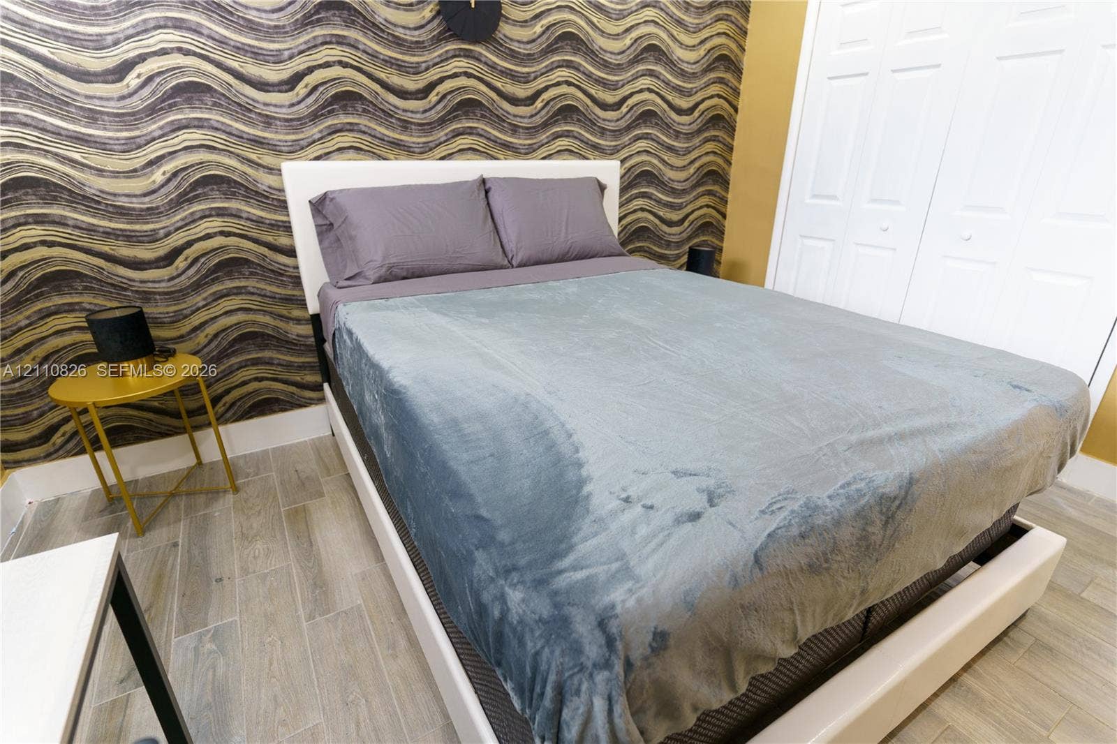 Textured gold and black accent wall, light-toned wood-finish tile flooring, and white double-panel closet doors