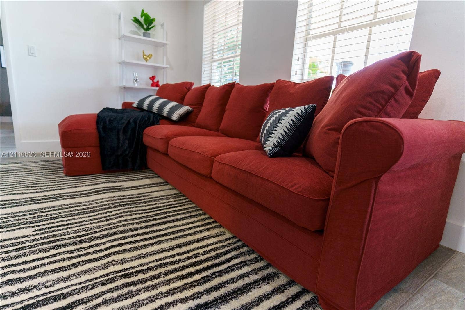 Room featuring neutral-toned walls, wood-finish flooring, and multiple windows fitted with horizontal blinds