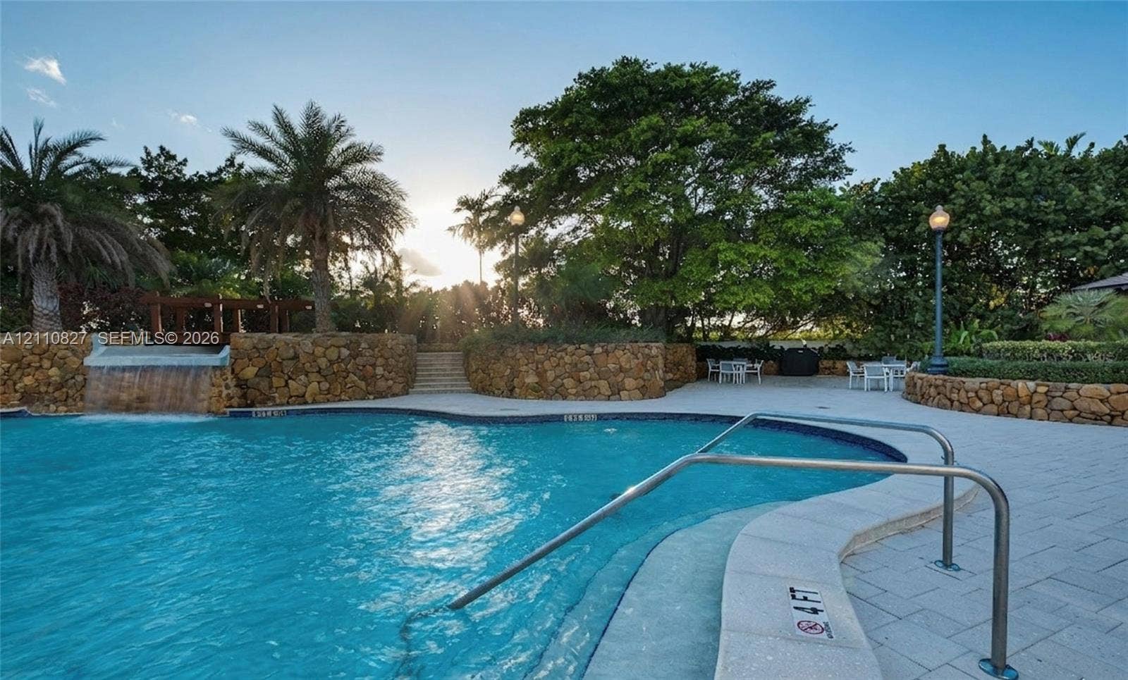 4000 Towerside Terrace, #908, Miami, Miami, FL 33138 Swimming pool featuring a rock-faced water feature, paver-stone decking, metal handrails, and surrounding mature landscaping