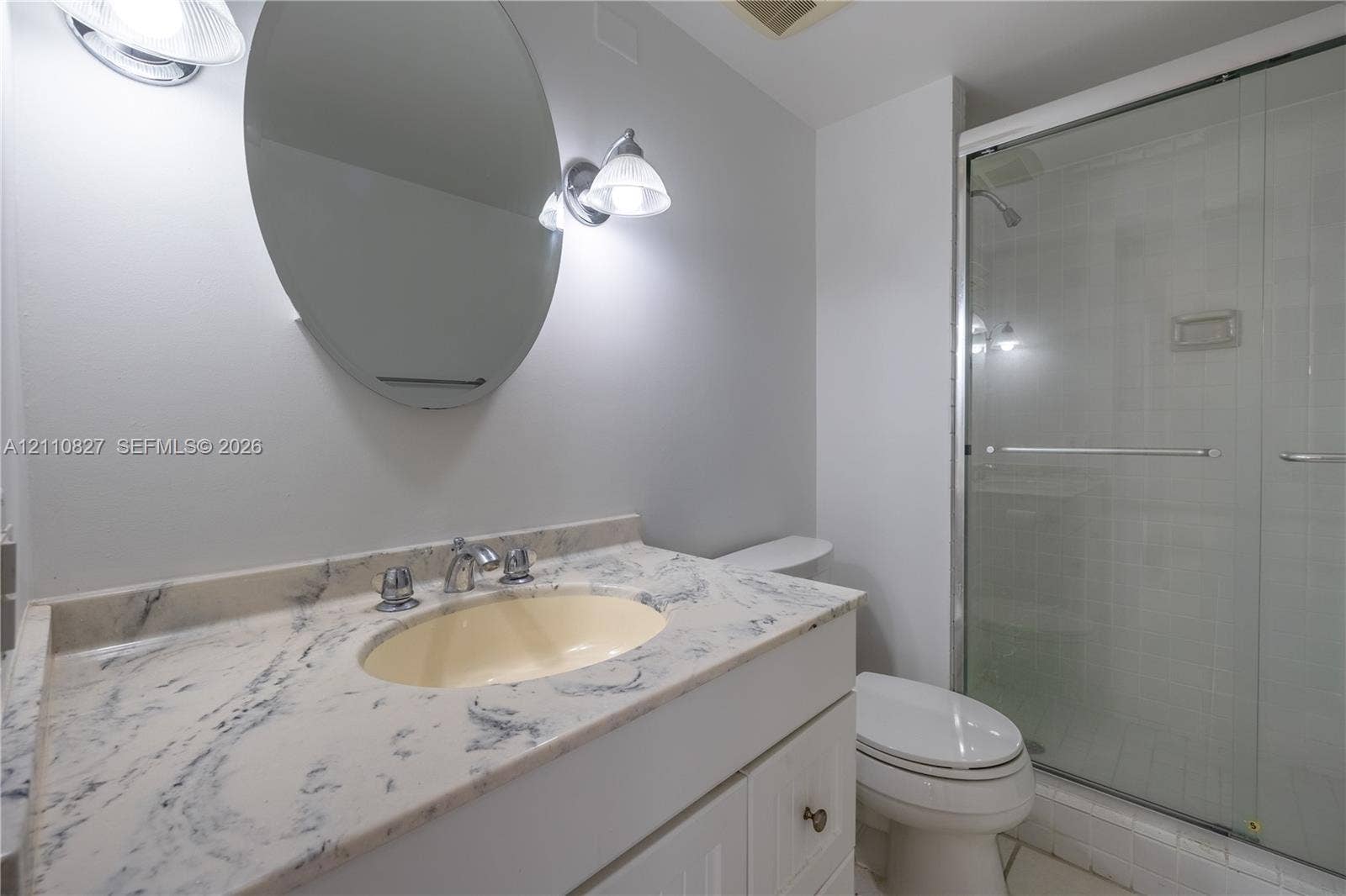 4000 Towerside Terrace, #908, Miami, Miami, FL 33138 Stone-surfaced vanity with an integrated oval sink, oval wall-mounted mirror, dual-light fixture, and glass-enclosed shower stall
