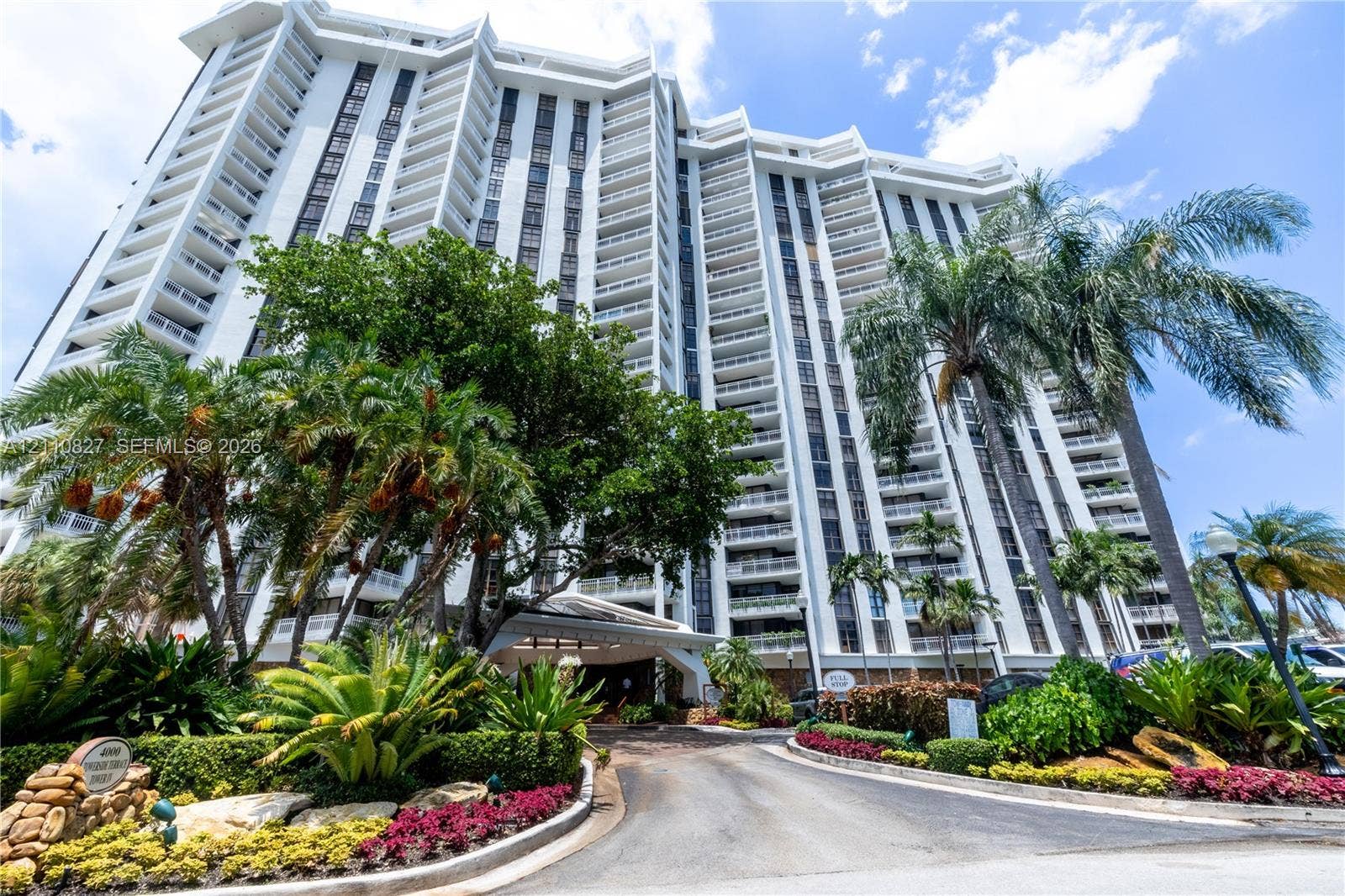 4000 Towerside Terrace, #908, Miami, Miami, FL 33138 High-rise residential exterior featuring stepped architectural balconies, white concrete facade, covered porte-cochere entry, and extensive tropical landscaping