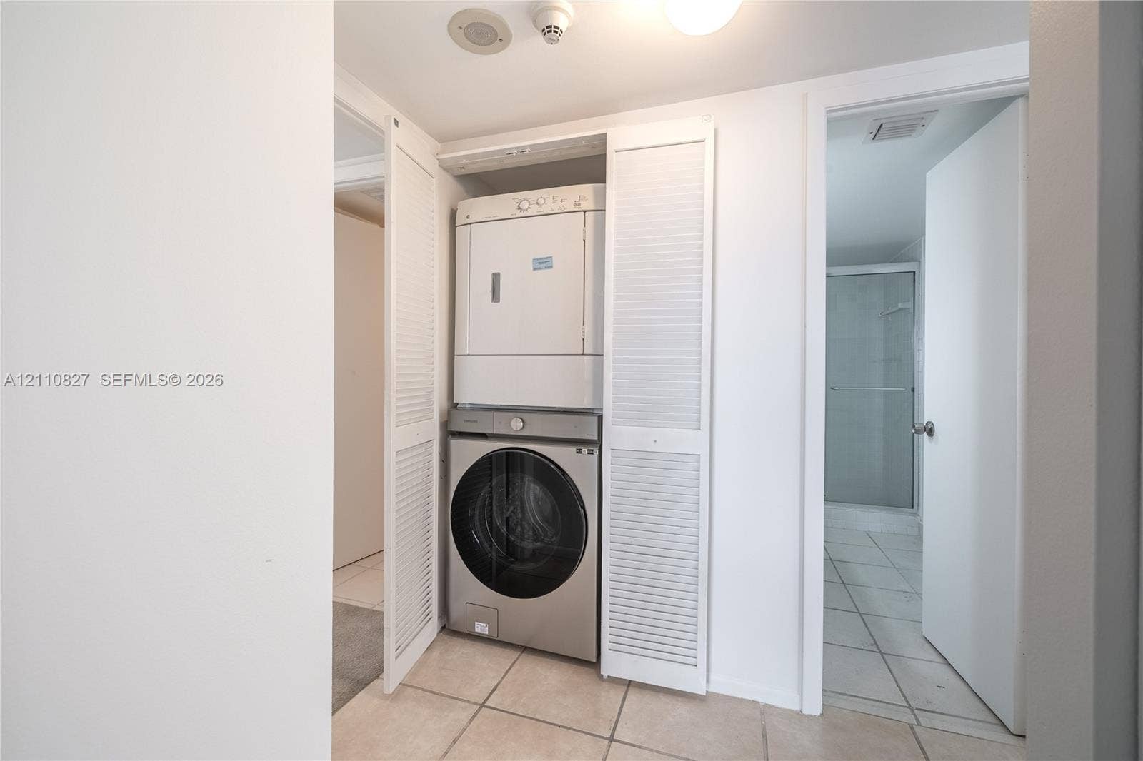4000 Towerside Terrace, #908, Miami, Miami, FL 33138 Laundry closet featuring white louvered bifold doors, stacked appliance configuration, and tile flooring