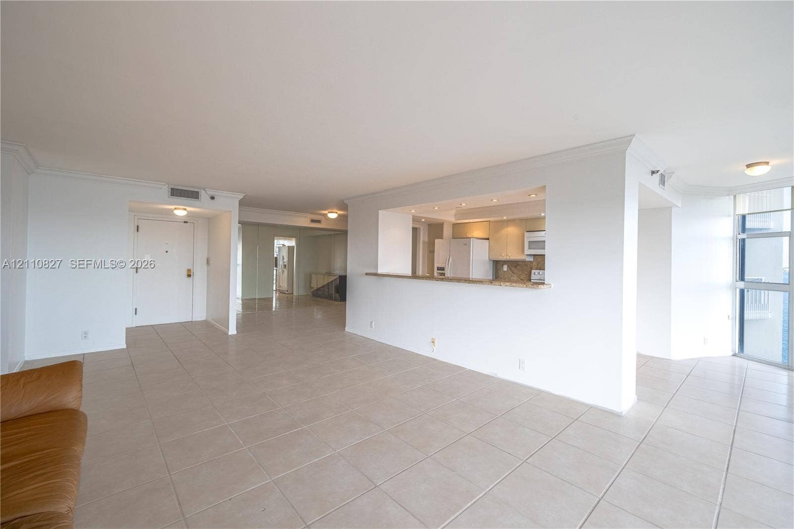 4000 Towerside Terrace, #908, Miami, Miami, FL 33138 Open-concept living space featuring large-format tile flooring, crown molding, kitchen pass-through with stone countertop, and full-height windows