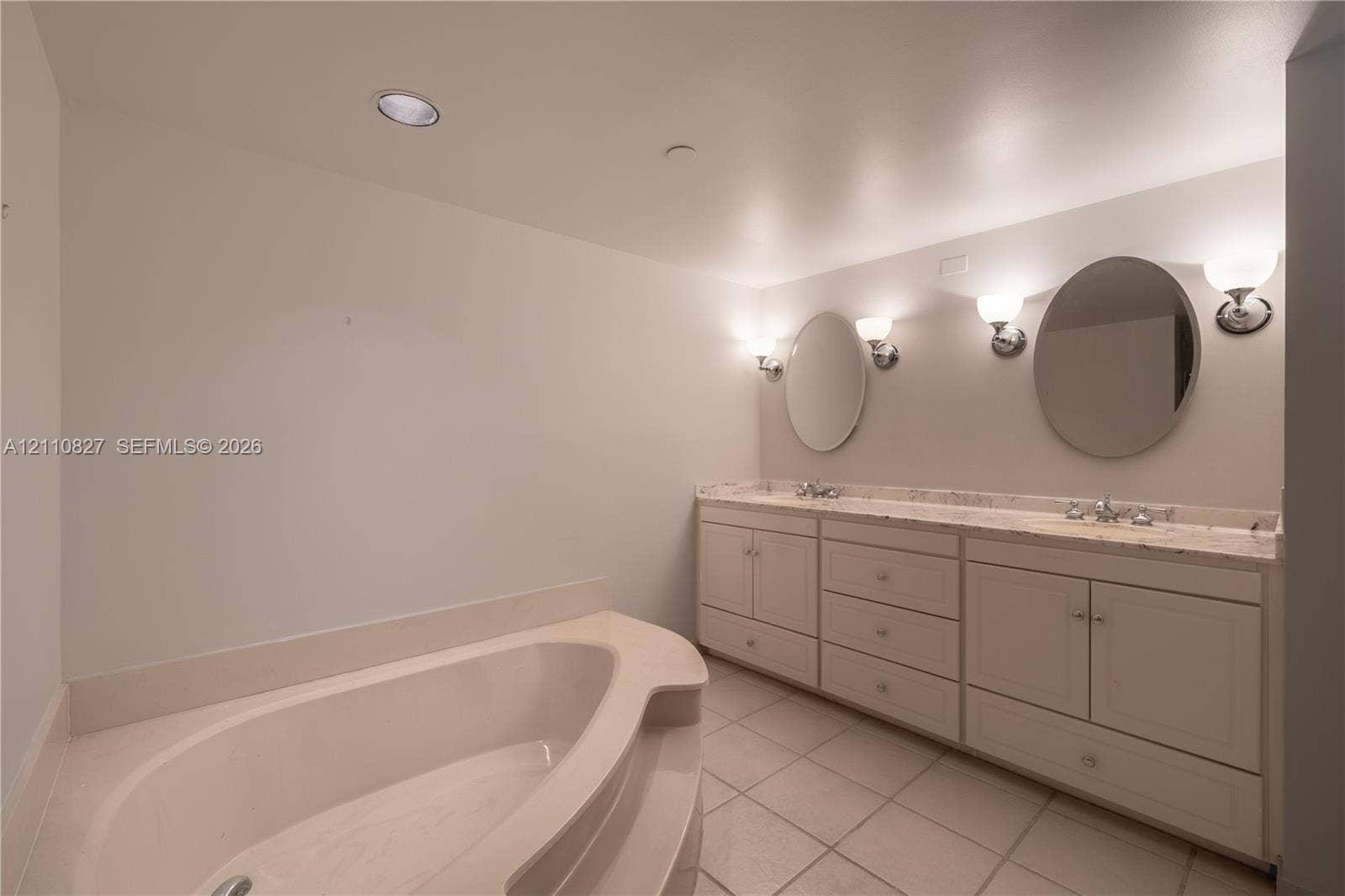 4000 Towerside Terrace, #908, Miami, Miami, FL 33138 Dual-sink vanity with stone-surfaced countertop, drop-in soaking tub, tile flooring, and wall-mounted round mirrors