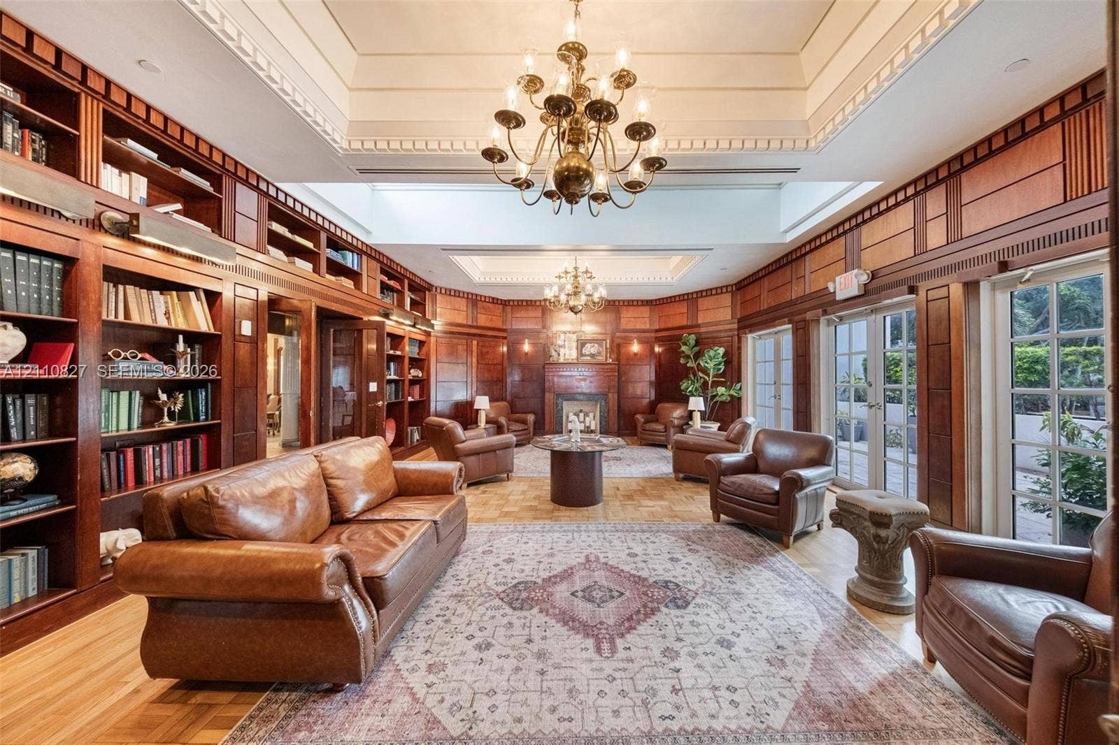 4000 Towerside Terrace, #908, Miami, Miami, FL 33138 Extensive floor-to-ceiling wood paneling, built-in library shelving, dual tiered tray ceilings with decorative millwork, multiple sets of glass-paneled doors, and a central fireplace with a wood mantel
